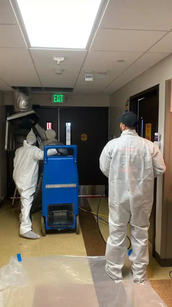 Technician cleaning ceiling vent in commercial hallway