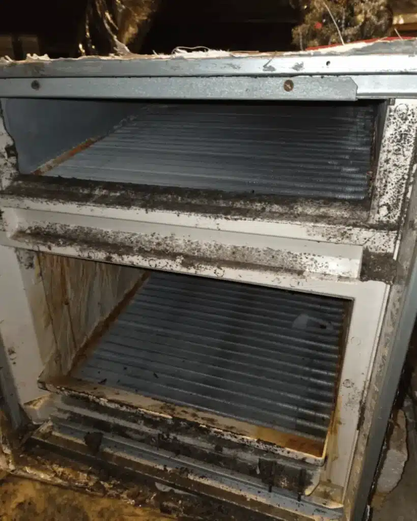 Close-up of dirty evaporator coil with heavy dust buildup and grime, showing the metal fins and buildup of debris