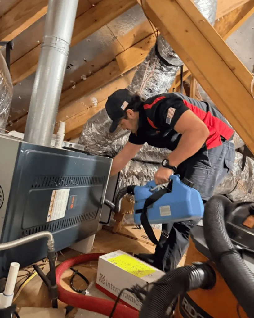 Technician performing HVAC system sanitizing treatment inside attic unit