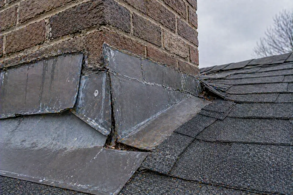 Damaged chimney flashing on roof with visible gaps and wear